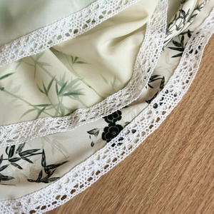 Detailed close-up of light green ink wash fabric with white lace trim and bamboo pattern