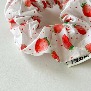 Close-up of floral fabric scrunchie with red strawberry patterns and FMdrea woven label