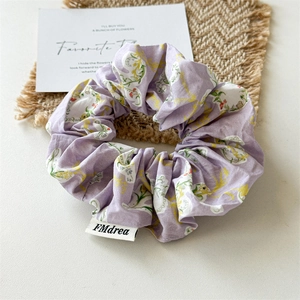 Close-up of a purple floral fabric scrunchie with yellow flower patterns on a woven mat