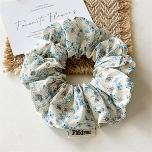 Close-up of floral fabric scrunchie with brand label on rustic straw mat background