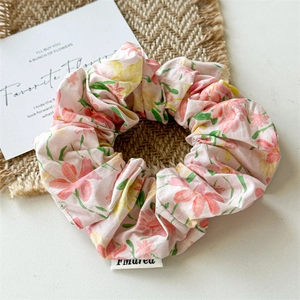 Detail of a light pink floral scrunchie with soft fabric texture and logo label