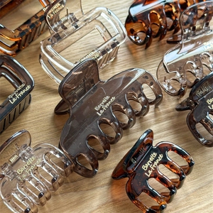 Minimalist brown resin shark hair claw clips with gold lettering on wood background