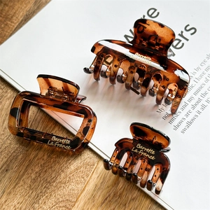 Three-piece set of tortoiseshell resin hair claws with golden logo on wooden background