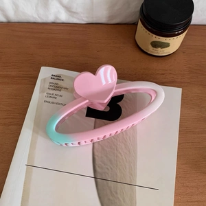 Close-up of pink and green gradient hair claw clip with heart decoration on a magazine