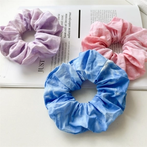 Close-up of three tie-dye scrunchies in purple, pink, and blue with soft cotton texture