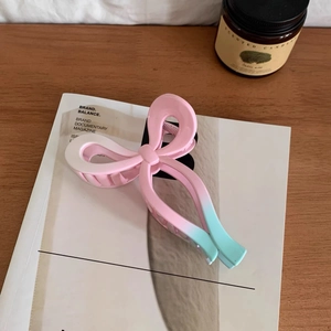 Detail of pink and mint green gradient bow-shaped hair claw clip on a stylish white magazine