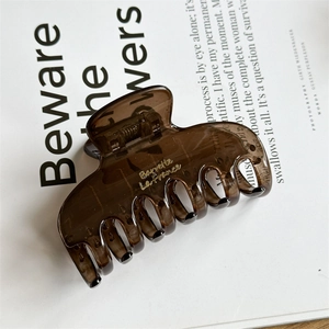 Detailed macro view of large dark brown resin hair claw clip with gold lettering