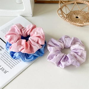 Close-up of three tie-dye fabric scrunchies in pink, blue and purple on a magazine