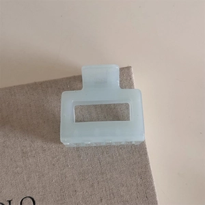 Detail of a minimalist light blue rectangular matte hair claw clip in a soft aesthetic setting