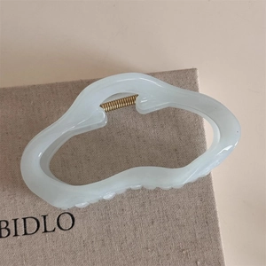 Macro view of a creamy white cloud-shaped hair claw clip with golden metal spring detail
