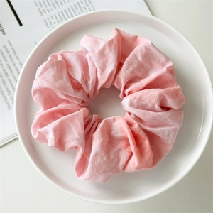 Close-up of a pale pink scrunchie with wrinkled fabric texture on a white tray
