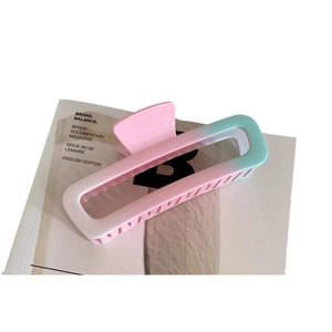 Rectangular hollow hair claw clip with pink and blue gradient on a minimalist magazine