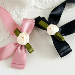 Detail of satin bow hair clips with white roses in pink and black on white lace