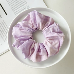 Close-up of a tie-dye purple and white cotton scrunchie on a white ceramic plate
