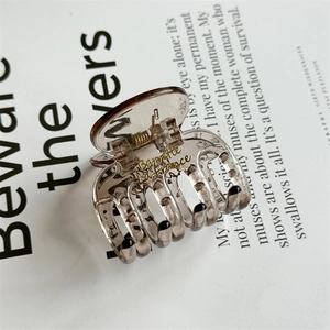Macro detail of brown resin hair claw clip with golden metal spring and inner engraving