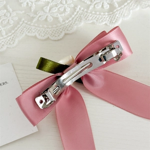 Pink satin ribbon bow hair clip with spring fastener shown on lace background