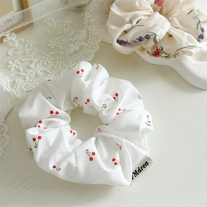 Detailed view of cherry print fabric scrunchie with Mdrea woven label on lace cloth