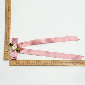 Pink satin ribbon bow with cream rose detail and long tails shown on a scale ruler