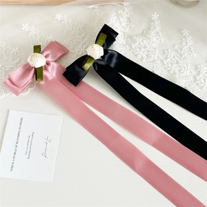 Detail of pink and black satin bow hair clips with delicate fabric rose and green leaf accents