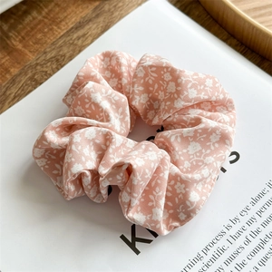 Detailansicht eines rosa geblümten Scrunchies mit weichem Stoff und Gänseblümchen-Muster