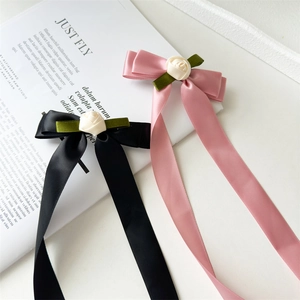 Close-up of elegant pink and black satin bow hair clips with cream rose and green leaf details