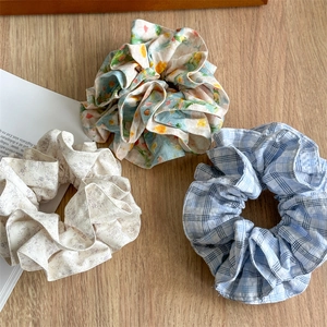 Three oversized fabric scrunchies in floral and plaid prints on light wood background