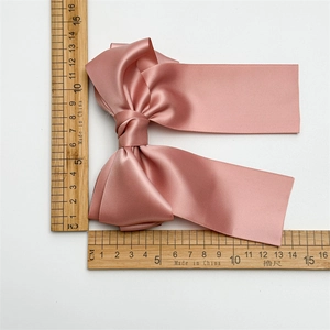 Détail d'une pince à cheveux nœud en satin rose avec rubans sur une règle graduée