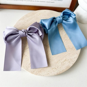Détail de barrettes à nœuds en satin de soie lilas et bleu sur un plateau en pierre