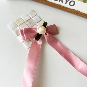 Close-up of handmade pink satin bow hair clip with white rose and green leaves