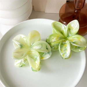 Detail of green and beige marble texture flower hair claw clips in a ceramic tray