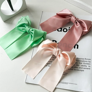 Détail de grandes barrettes à nœuds en satin rose, vert et beige clair soyeux