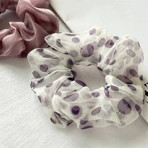 Dettaglio di scrunchie in organza bianca a pois viola e elastico in raso di seta rosa