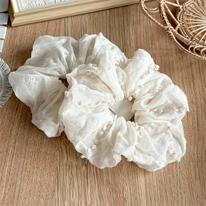 Detail of cream white fabric scrunchies with floral embroidery and soft pom-pom trim texture