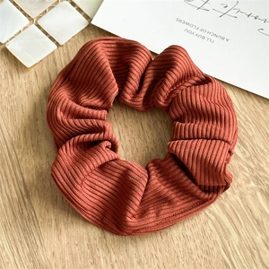 Detailed texture of brick red striped knit scrunchie on a natural wooden background