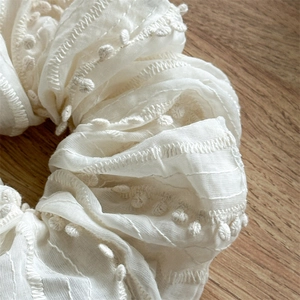 Detailed macro view of white fabric scrunchie with delicate pompom edge on wood background