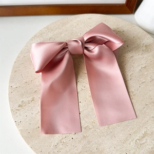 Détail d'une pince à cheveux nœud en satin rose avec longs rubans sur support pierre