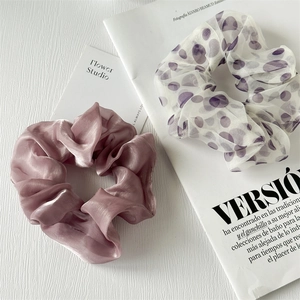 Dettaglio di elastici per capelli in seta rosa e organza a pois bianchi su fondo legno