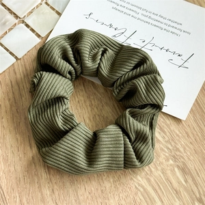 Close-up of army green striped fabric scrunchie on a wooden surface with aesthetic decor