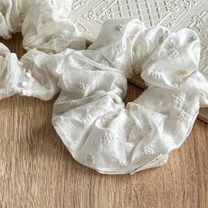 Detail of white floral embroidery on a soft pleated cream fabric scrunchie