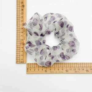 Scrunchie in organza a pois viola mostrato con un righello in legno per confronto taglie
