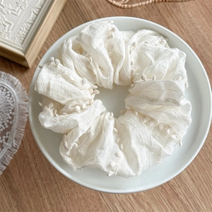 Close-up of cream white fabric hair scrunchie with mini pom-pom trim and wavy stitching