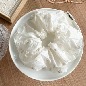 Detail of cream white fabric scrunchie with floral embroidery and brand label