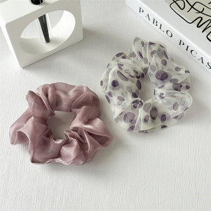 Dettaglio di scrunchie in seta lavanda ed elastico in organza a pois su scrivania moderna