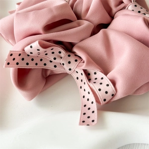 Detail of pink satin scrunchie with a black polka dot bow ribbon on a white tray