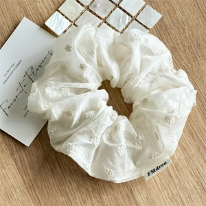 Detail shot of a white fabric scrunchie with floral embroidery and brand woven label