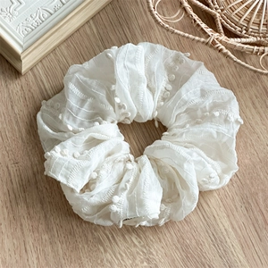 Detail of white fabric scrunchie with floral embroidery and textured tulle finish