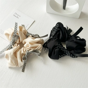 Close-up of silk-like polka dot bow scrunchies in cream and black on a white surface