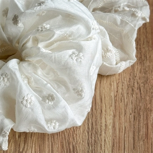 Close-up of cream white fabric scrunchie with delicate floral embroidery on wood background