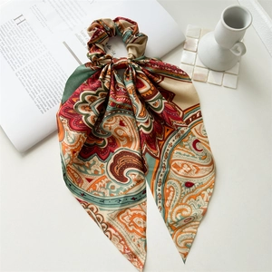 Detail of silk paisley print scrunchie with long scarf streamers on minimal white background