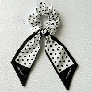 Détail d'un chouchou à pois noirs et blancs avec de longs rubans sur une surface texturée